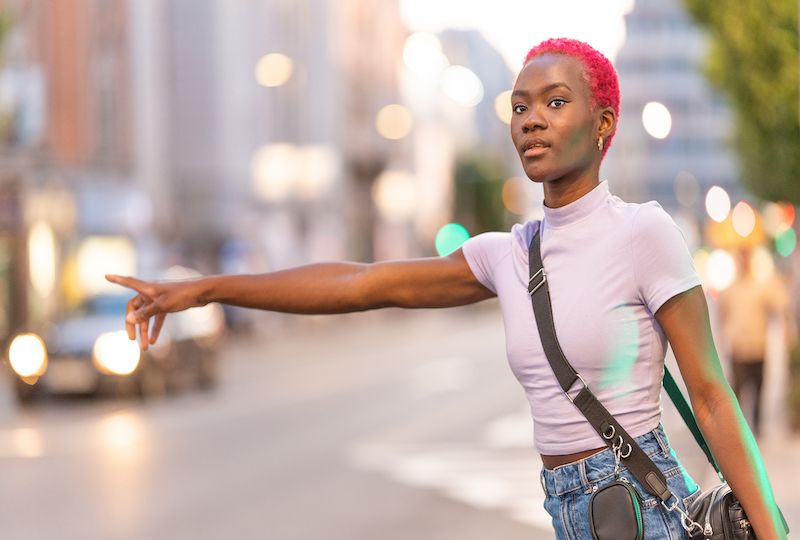 African woman with short pink hair hairstyle hailing a taxi in the street