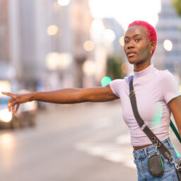 Stylish young african woman with short pink hair hairstyle hailing a taxi in the city